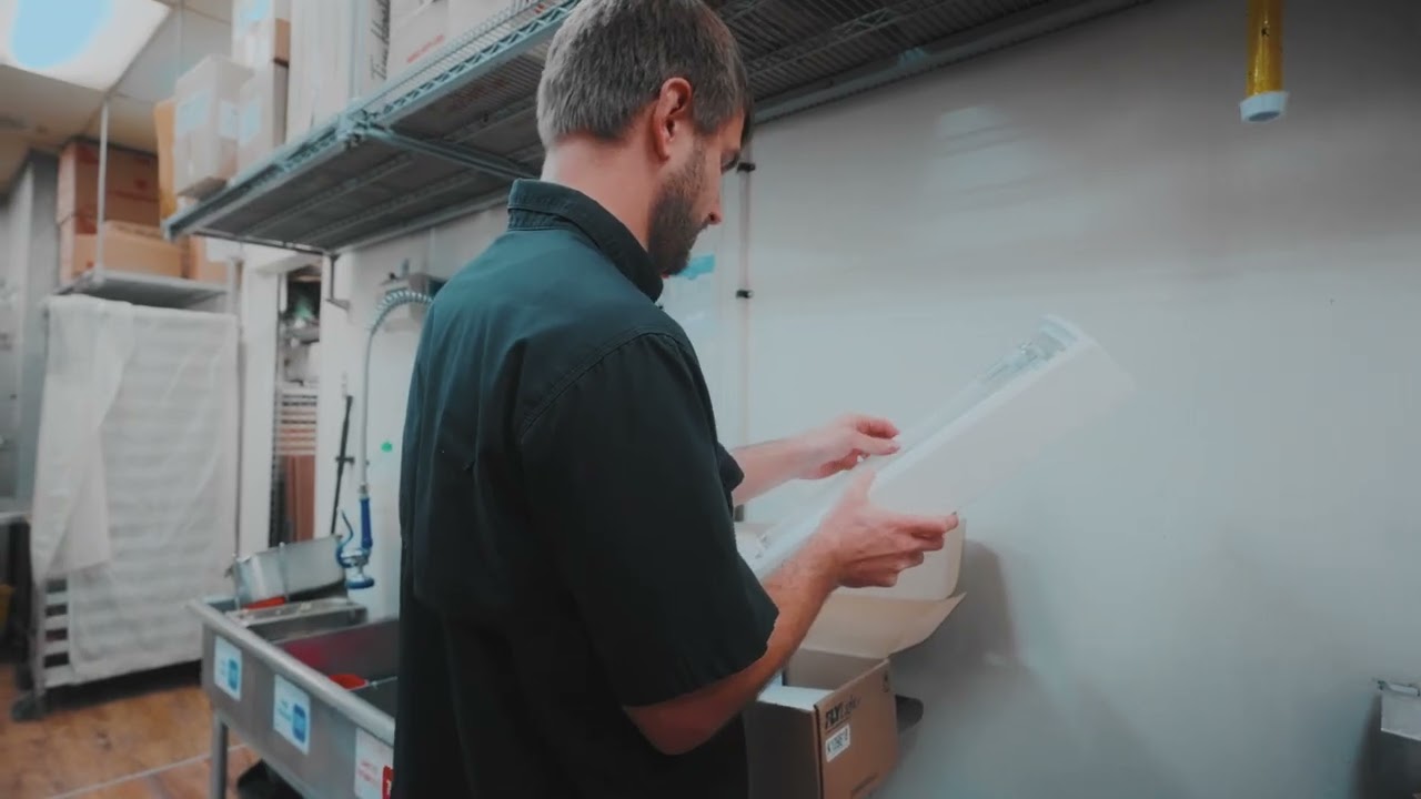 A Phantom Pest Control technician reviewing paperwork in a back-of-house storage room with steel shelving and cartons