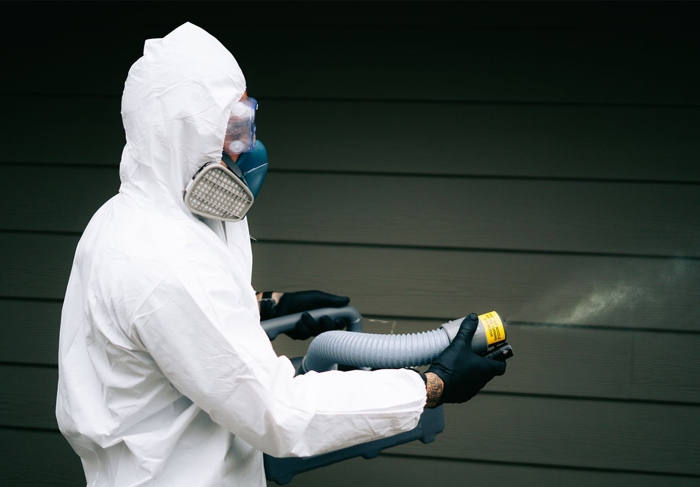 A Phantom Pest Control technician in a white protective suit and respirator holding treatment equipment