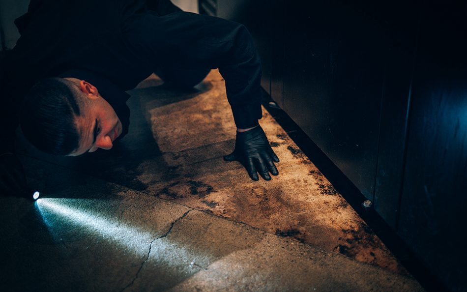 Phantom Pest Control technician kneeling with a flashlight to inspect a dark, low space