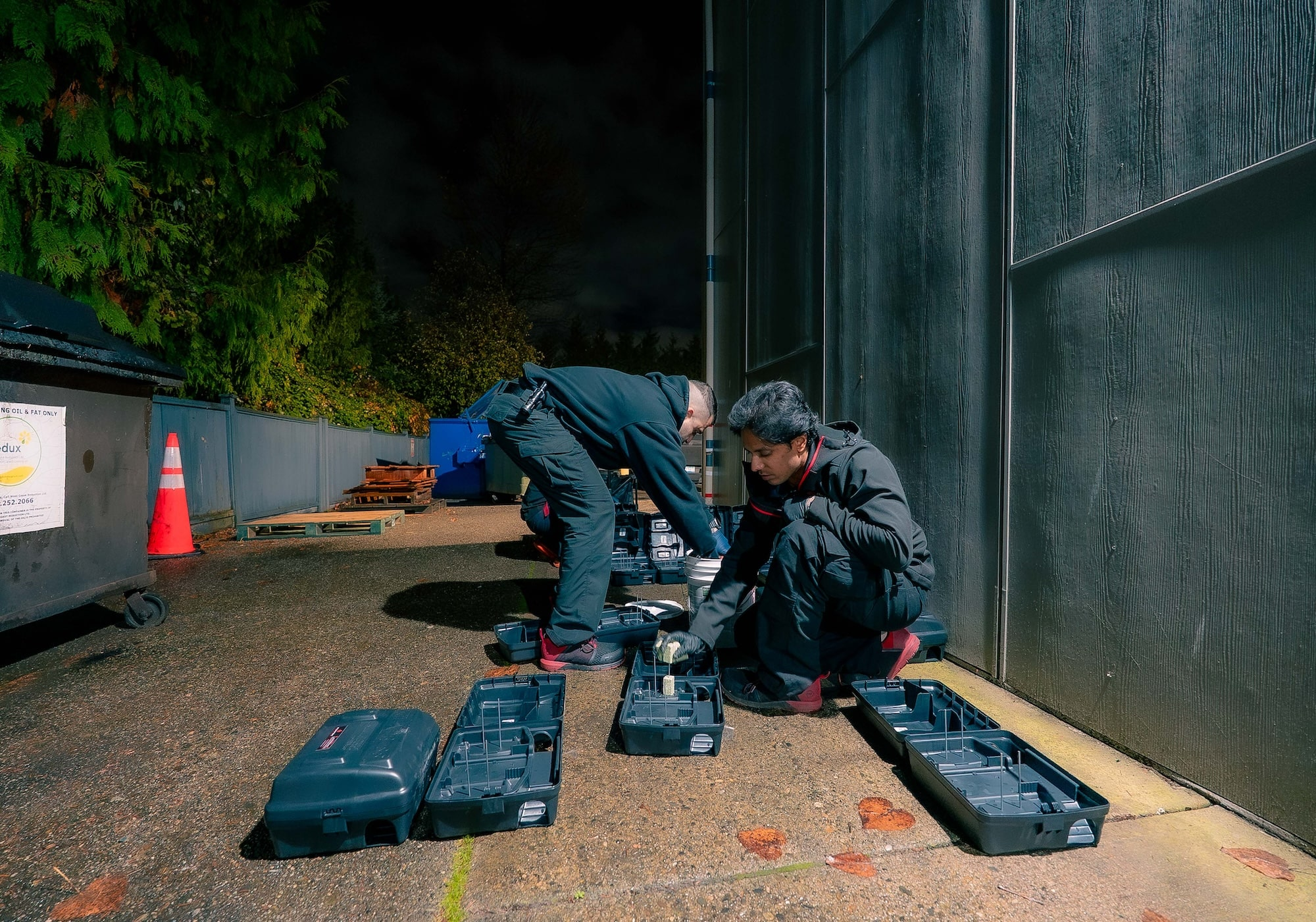 Two Phantom Pest Control technicians setting up rodent bait stations along a commercial building’s service lane