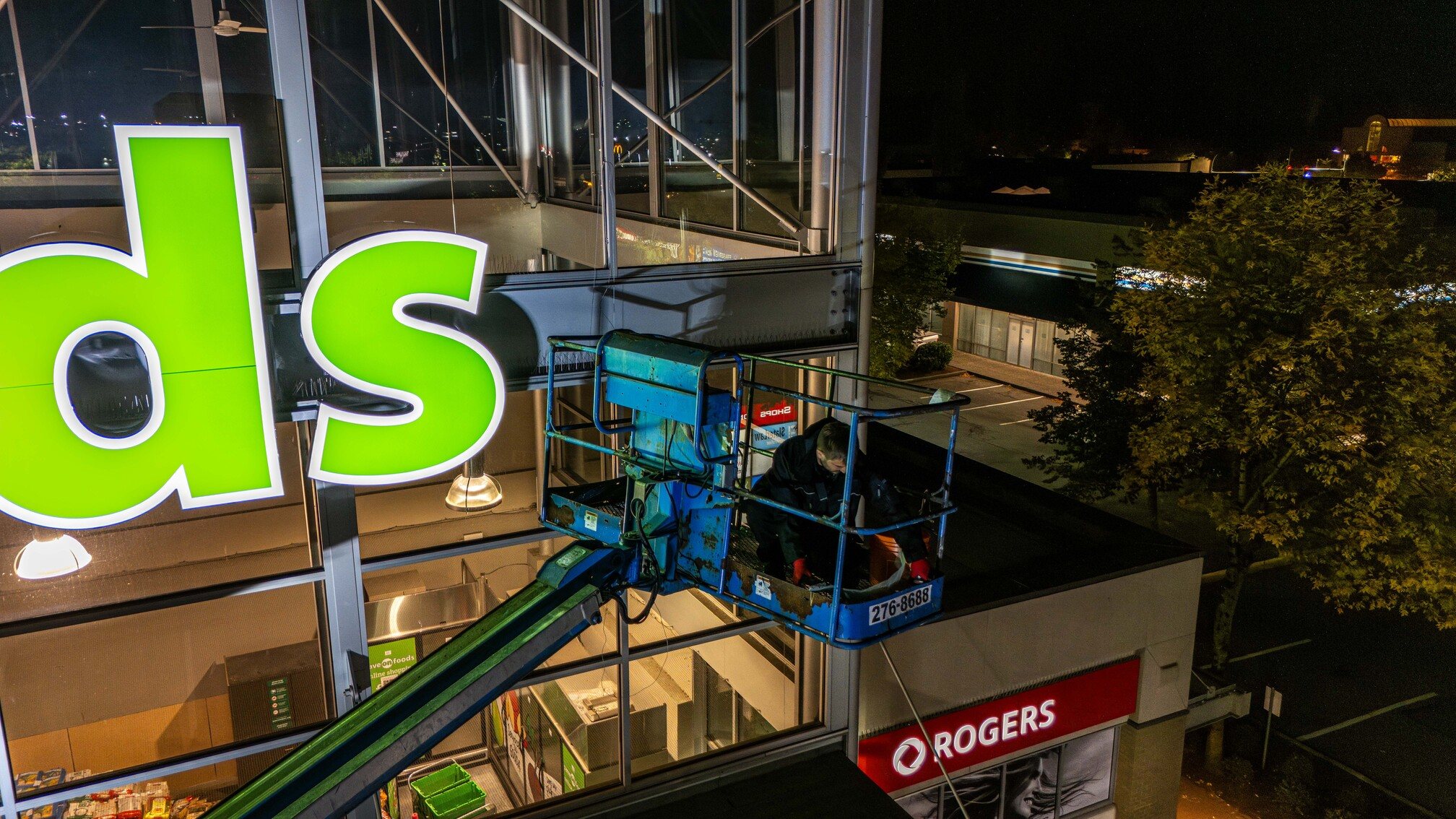 A Phantom Pest Control technician on a boom lift at the upper storey of a commercial building at night