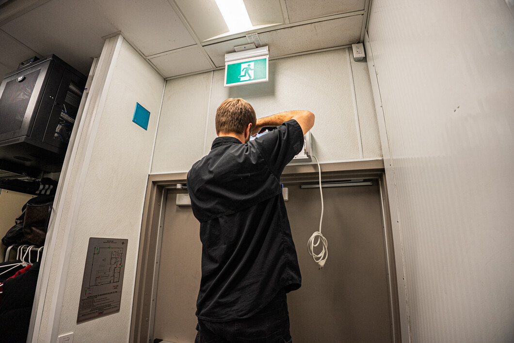 Phantom Pest Control technician checking a wall-mounted fixture above a back exit door in a commercial staff corridor